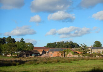 A row of old red brick buildings with ploughed fields beyond