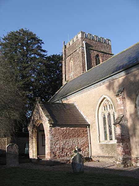 A large red stone church with a porch entrance from the churchyard