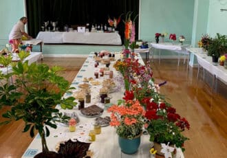A long white table with an array of potted and vased flowers, and a selection of homemade cakes, jams and preserves.