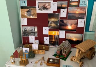 A table full of beautiful crafts, including a wagon and a small model greenhouse. A board behind is full of photos of sunsets