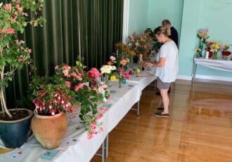 A long table of potted plants and flowers in vases, set up to be judged.