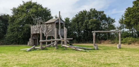 A large wooden play structure in a recreational field.