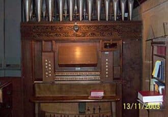An old wooden church organ, with pipes above and engraved wooden cornicing.