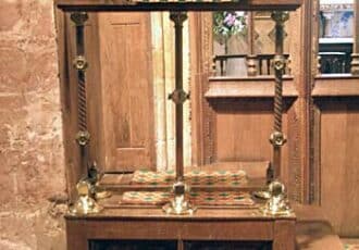 A wooden pulpit with engraved details. A green penant hands down with a cross in the centre.